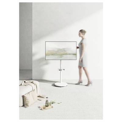 Eine Person in einem grauen Kleid steht neben einem modernen Fernseher auf einem minimalistischen Ständer in einem hellen, luftigen Raum mit neutralen Tönen.