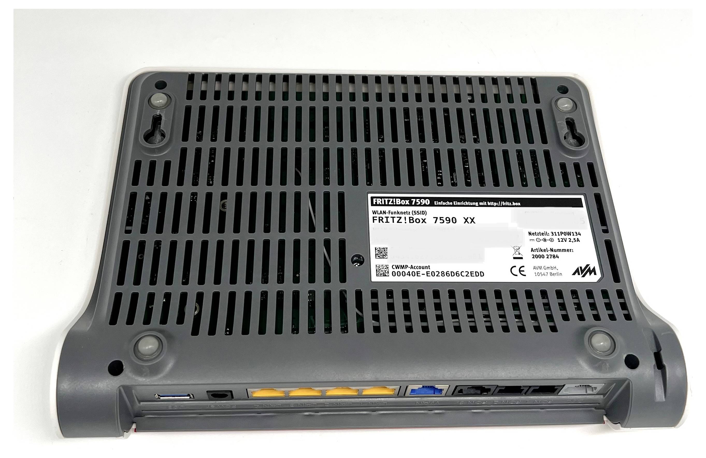 Die Unterseite eines FRITZ!Box 7590-Routers, die Belüftungsschlitze, ein Modell- und Seriennummern-Etikett sowie Anschlüsse für Netzwerkverbindungen zeigt.