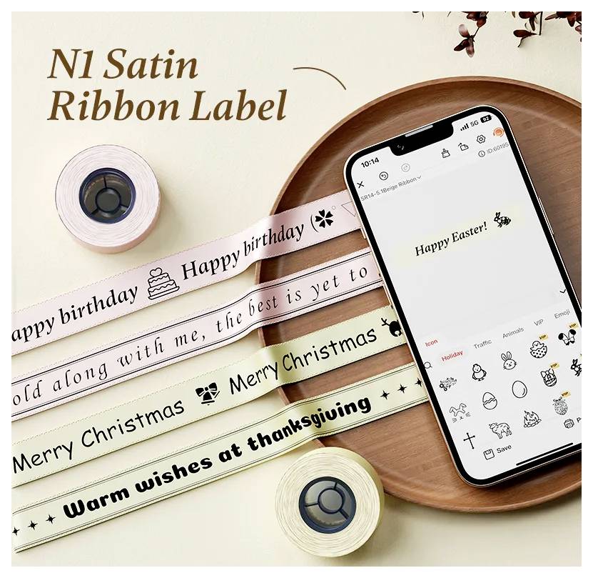 Flache Anordnung von Satinband-Etiketten für Feiertage und Geburtstage neben einem Telefon, das eine Oster-Nachricht und eine Label-Design-App anzeigt.