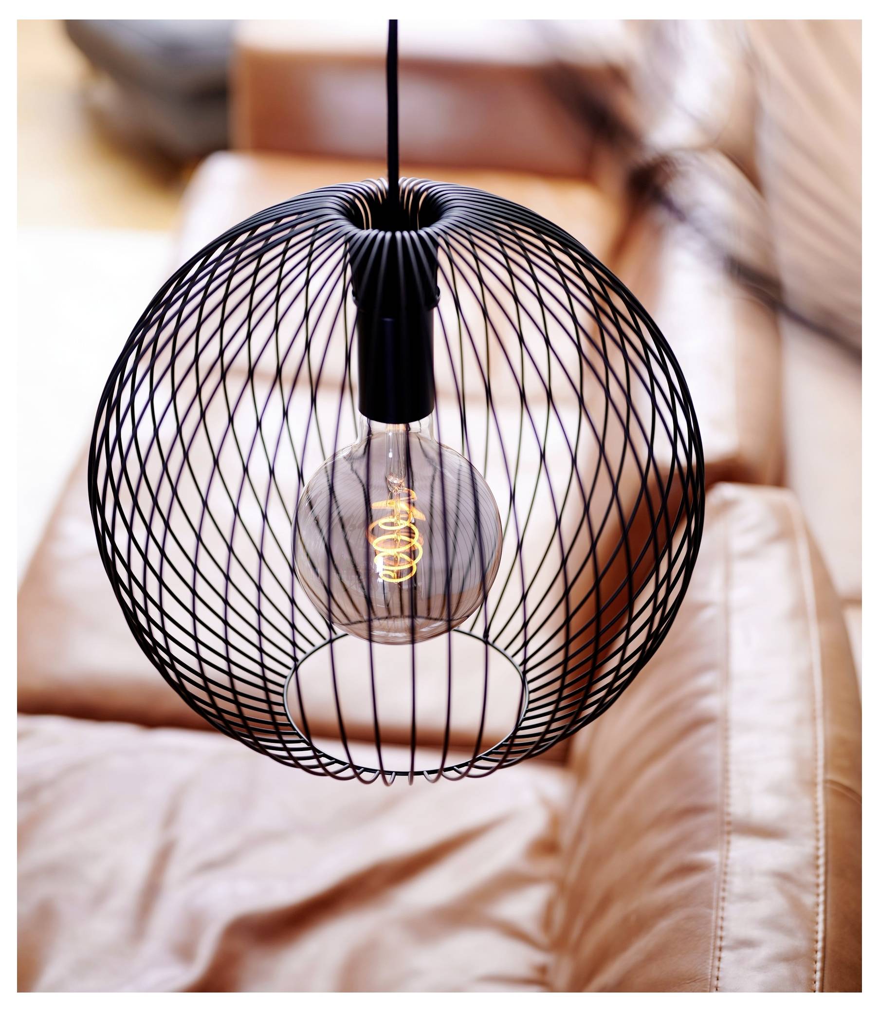 „Schwarze Draht-Pendelleuchte mit einer sichtbaren LED-Glühfadenbirne über einem braunen Ledersofa in einem modernen Wohnraum."