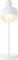 Eine moderne weiße Tischlampe mit zylindrischem Schirm und schlankem Fuß, beleuchtet mit einer sichtbaren Glühbirne, auf neutralem Hintergrund.