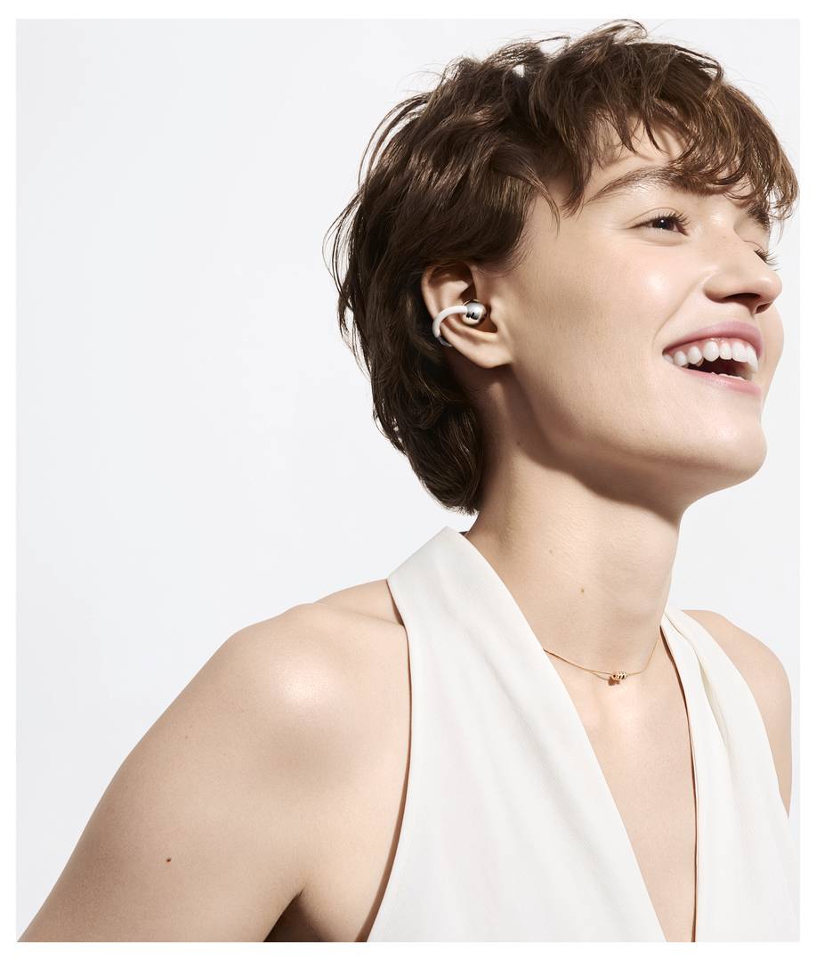 Eine Person mit kurzen Haaren lächelt, während sie kabellose Ohrhörer trägt, was auf Freude an Musik oder Audio hindeutet, gekleidet in ein ärmelloses Oberteil.