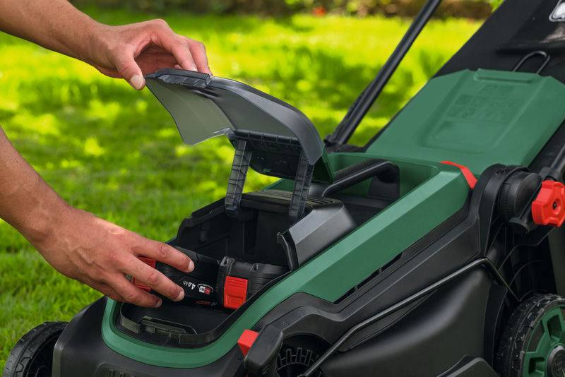 Eine Person setzt einen Akku in einen kabellosen Rasenmäher mit grünem und schwarzem Design ein, was seinen umweltfreundlichen Betrieb unterstreicht.