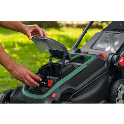 Eine Person setzt einen Akku in einen kabellosen Rasenmäher auf einer grasbewachsenen Wiese ein und bereitet das Gerät für die Verwendung vor.