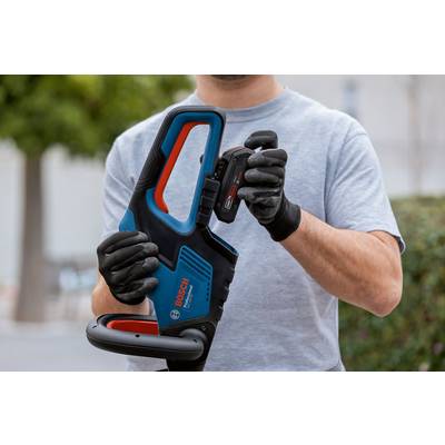 Eine Person mit Handschuhen setzt eine Batterie in ein Bosch-Elektrowerkzeug ein, wobei der Fokus auf Einrichtung und Betrieb liegt, mit Grünflächen im Hintergrund.