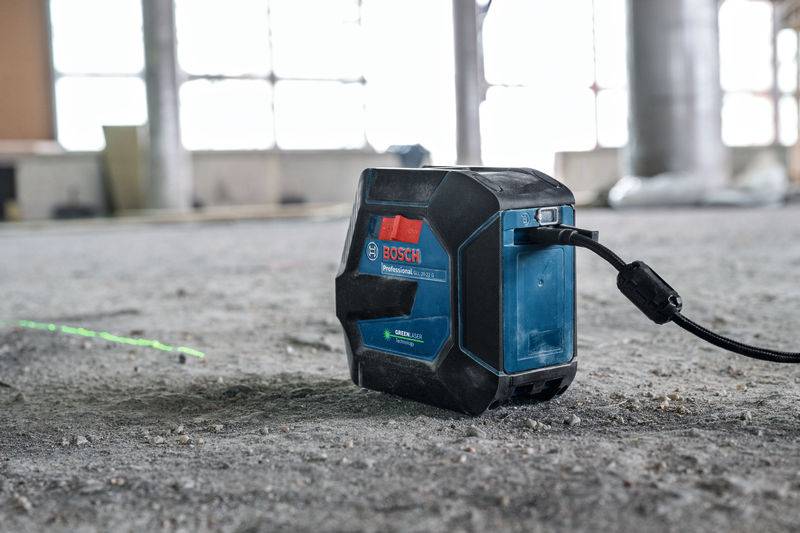 Ein Bosch-Lasernivellier projiziert eine grüne Linie auf einen Betonboden auf einer Baustelle und zeigt damit präzises Nivellieren für Bauarbeiten an.