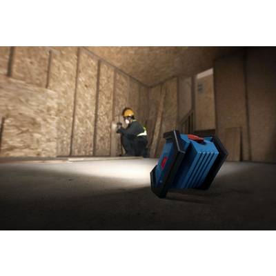 Ein Bauarbeiter mit Schutzhelm und Weste macht ein Foto in einem unfertigen Holzrahmenzimmer, während eine blaue tragbare Leuchte im Vordergrund steht.