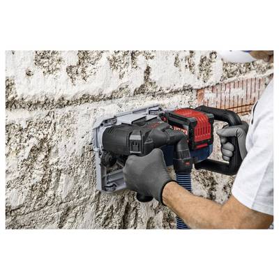Arbeiter, der eine Wandschneidesäge verwendet, um eine Nut in eine Beton- oder Steinwand zu schneiden, hält das Werkzeug mit behandschuhten Händen, während sich Staub um den Schnitt ansammelt.