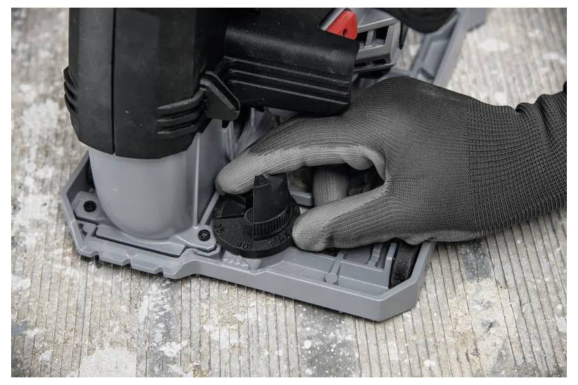 Behandschuhte Hand stellt den Tiefenregler an einem tragbaren Elektrowerkzeug ein, das auf einer Basis auf einer abgenutzten Holzwerkoberfläche montiert ist.