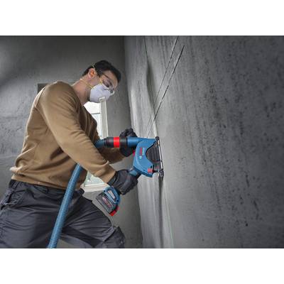 Eine Person in Schutzausrüstung verwendet ein Elektrowerkzeug an einer Betonwand und konzentriert sich auf die präzise Ausrichtung von Linien. Sonnenlicht fällt durch ein nahegelegenes Fenster ein.
