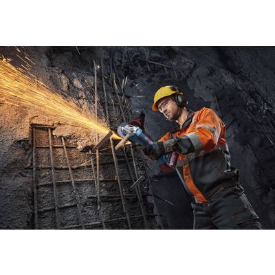 Ein Bauarbeiter in Schutzausrüstung nutzt einen Winkelschleiffer, um Metallbewehrung zu schneiden und erzeugt dabei Funken in einer schwach beleuchteten industriellen Umgebung.