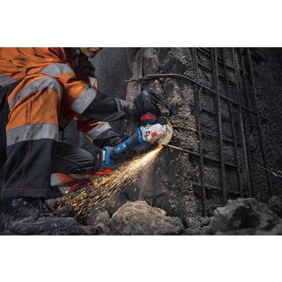 Ein Bauarbeiter in orangefarbener Schutzausrüstung benutzt ein Elektrowerkzeug, um Bewehrungsstahl an einer Betonwand zu schneiden, wobei helle Funken entstehen.