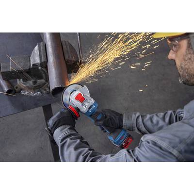 Eine Person trägt Handschuhe und Schutzausrüstung und verwendet einen Winkelschleifer, um ein Metallrohr durchzuschneiden, wobei in einer Werkstatt helle Funken entstehen.