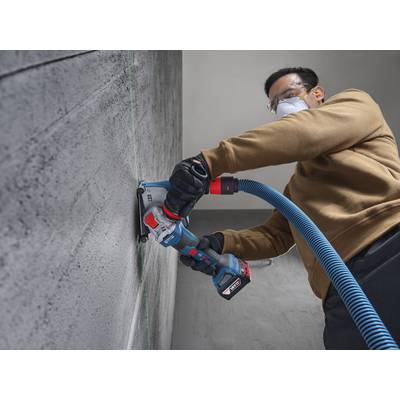 Eine Person in Schutzausrüstung verwendet ein Elektrowerkzeug, um eine Linie in eine Betonwand in einem Innenraum zu schneiden.