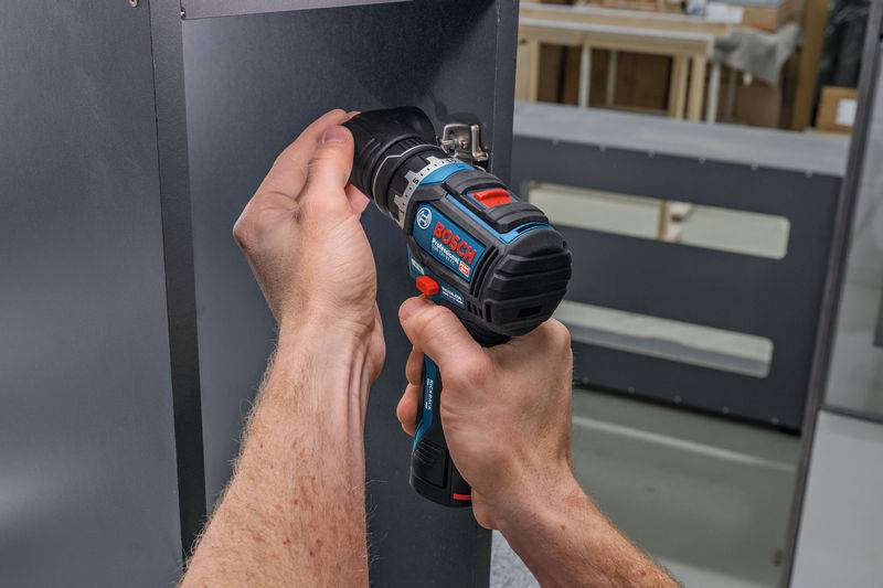 Eine Person benutzt eine Elektrobohrmaschine, um Schrauben in eine Metalloberfläche einzudrehen und zeigt dabei eine DIY- oder Reparaturaufgabe in einer Werkstattumgebung.