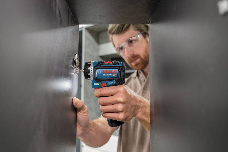 Eine Person nutzt ein Elektrowerkzeug von Bosch zum Verschrauben eines Panels, trägt dabei eine Schutzbrille und konzentriert sich auf die Aufgabe in einer Innenumgebung.