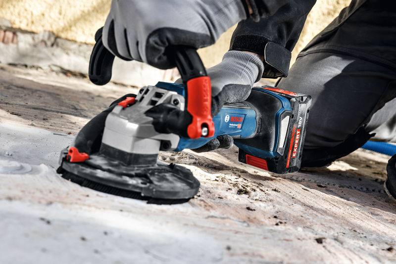Eine Person verwendet ein Bosch-Elektrowerkzeug zum Schleifen einer Betonoberfläche, trägt Schutzhandschuhe und betont damit Konstruktions- oder Renovierungsarbeiten.