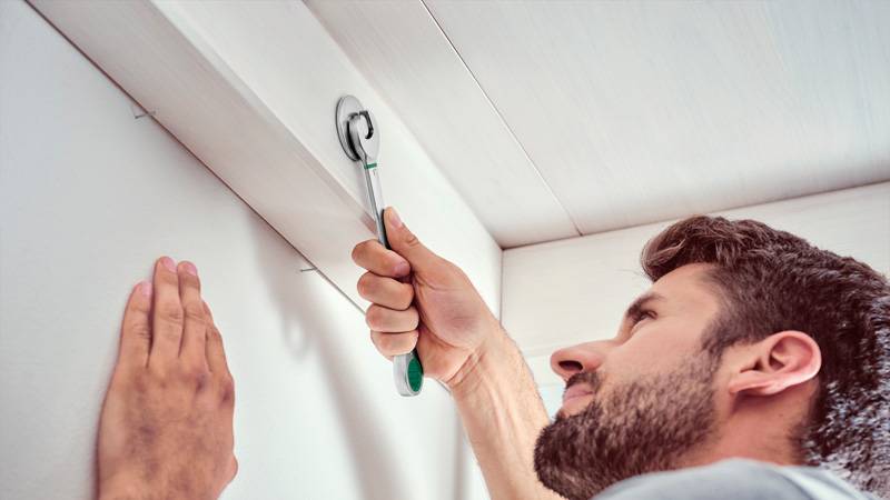 Eine Person installiert eine Sicherheitskamera in der Ecke einer Decke und verwendet einen Schraubendreher, um die Halterung einzustellen.