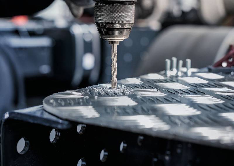 Ein Bohrer dringt in eine Metalloberfläche ein und erzeugt dabei spiralförmige Späne. Die Umgebung sieht nach einer industriellen oder Werkstattumgebung aus.