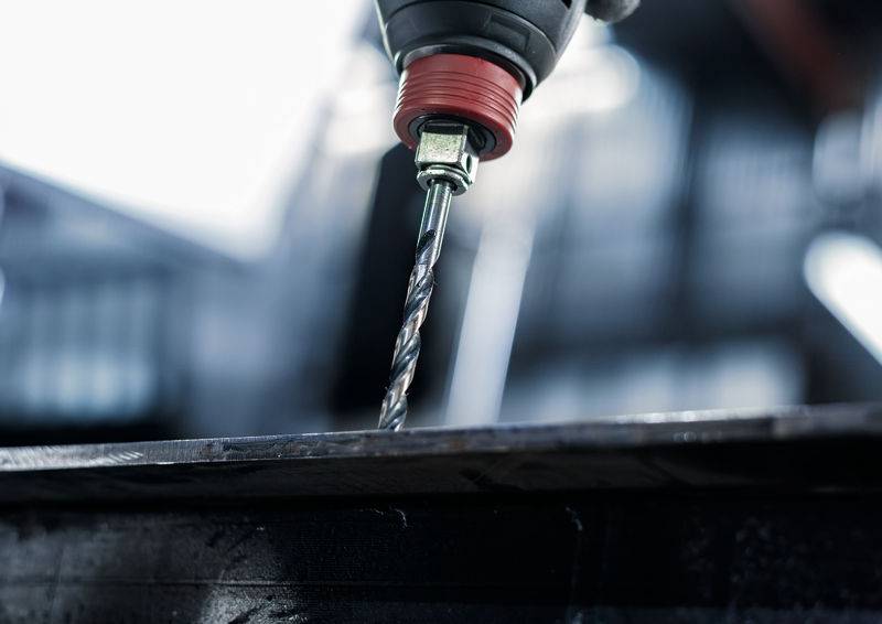 Eine Nahaufnahme eines Bohrers, der in eine Metalloberfläche eindringt, erfasst die Bewegung und konzentriert sich auf den Bohrmeißel, mit einem unscharfen Hintergrund.