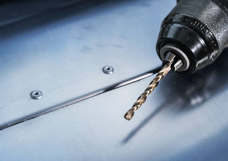 Eine Nahaufnahme einer Elektrobohrmaschine mit einem Metallbohrer, auf einer metallischen Oberfläche mit sichtbaren Schrauben platziert, wobei die Details des Werkzeugs hervorgehoben werden.