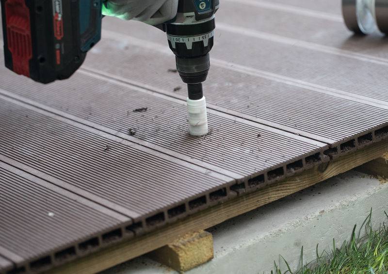 Bohrmaschine mit Lochsäge, die in ein Holzdeckbrett bohrt und Holzspäne um das Loch hinterlässt.