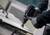 Eine Person bedient einen Elektroschrauber mit einem Lochsägen-Aufsatz auf einem leichten Holzbrett und trägt Handschuhe für die Sicherheit.