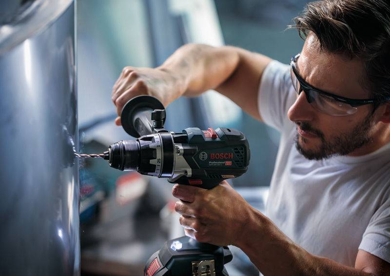 Eine Person, die einen Bosch-Elektroschrauber auf einer Metalloberfläche verwendet, trägt Schutzbrille und konzentriert sich auf präzises Bohren.