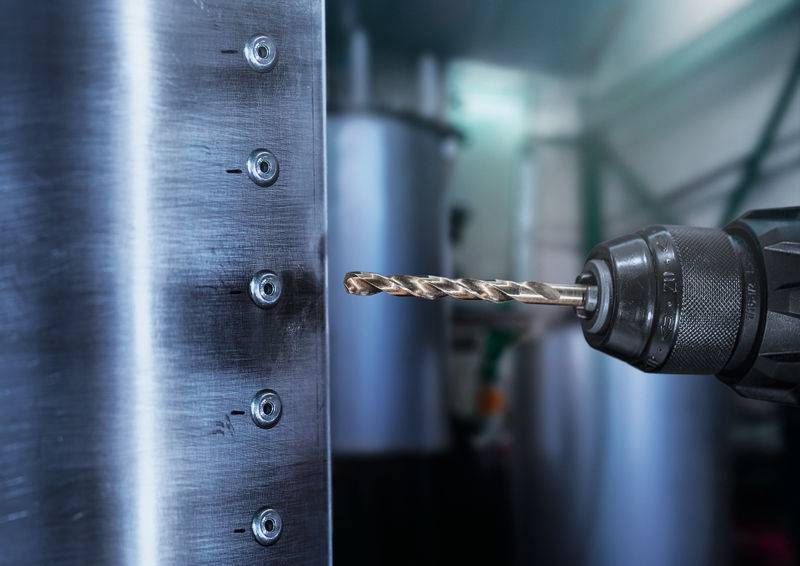 Eine Nahaufnahme eines Bohrers, der Löcher in eine Metalloberfläche bohrt, mit unscharfen Maschinen im Hintergrund, die eine industrielle Umgebung suggerieren.