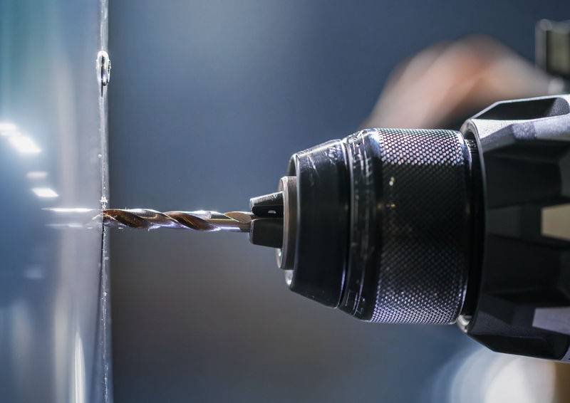 Eine Großaufnahme eines Bohrers, der in eine Metalloberfläche eindringt, und fängt die Bohrwirkung ein. Der Bohrer ist teilweise sichtbar und zeigt seinen strukturierten Griff.
