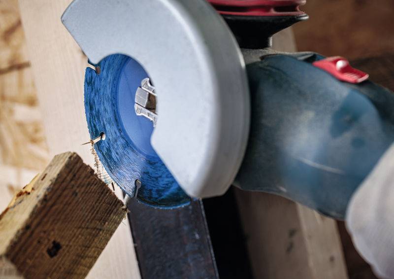 Ein Elektrowerkzeug mit einer blauen Schneidescheibe wird verwendet und schneidet durch ein Holzbrett.