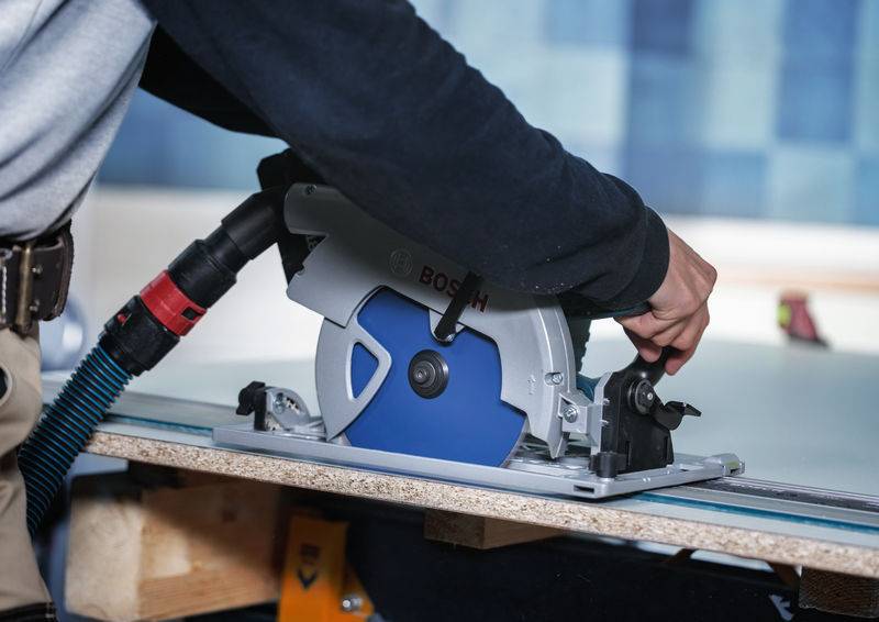 Eine Person bedient eine Bosch-Kreissäge zum Zuschneiden eines Holzblattes und hebt eine Holzbearbeitungssituation hervor. Die Säge hat eine blaue Blattabdeckung.