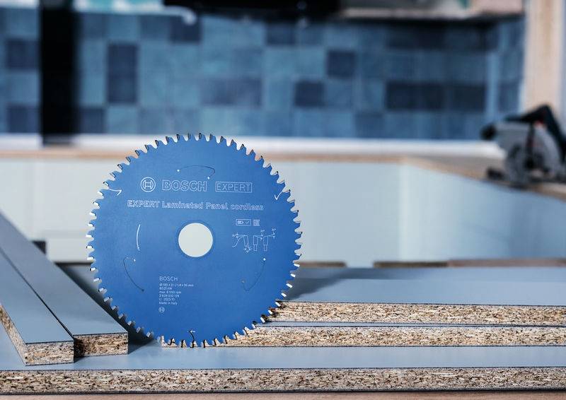 „Ein aufrecht stehendes Sägeblatt einer Kreissäge mit der Aufschrift „Bosch Expert for Laminated Panel" auf einem Stapel von Sperrholz, mit einer Werkstatt im Hintergrund."