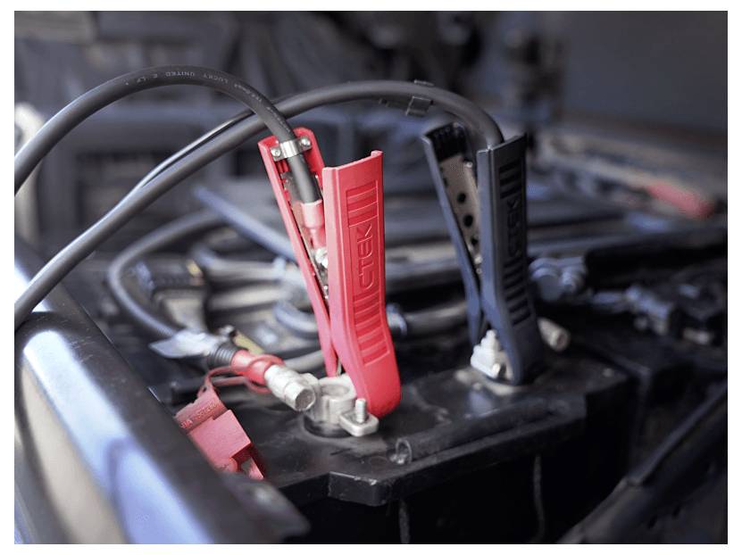 Autobatterie mit roten und schwarzen Starthilfekabeln, die an den Anschlüssen befestigt sind