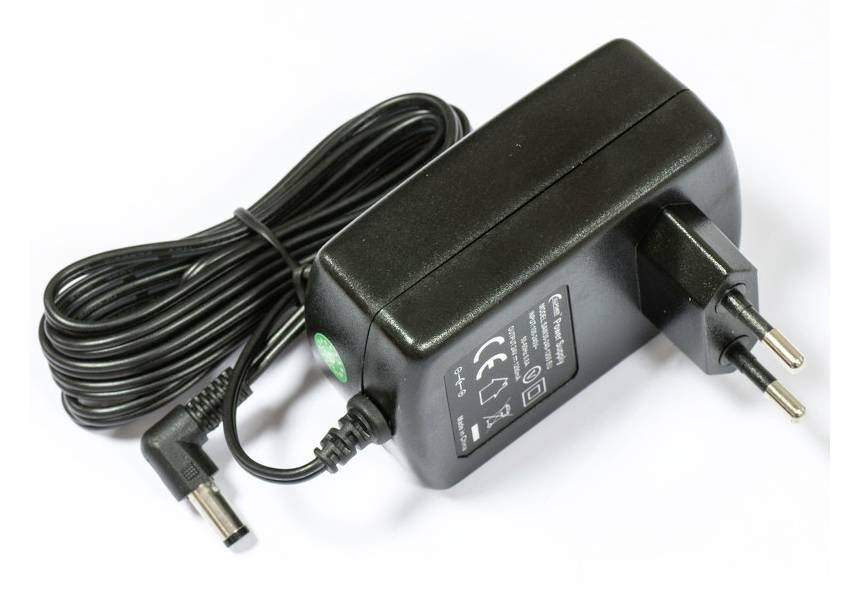 Ein schwarzer Stromadapter mit europäischem Stecker und aufgerolltem Kabel ruht auf einer einfachen weißen Oberfläche und zeigt die Spezifikationen auf dem Etikett.