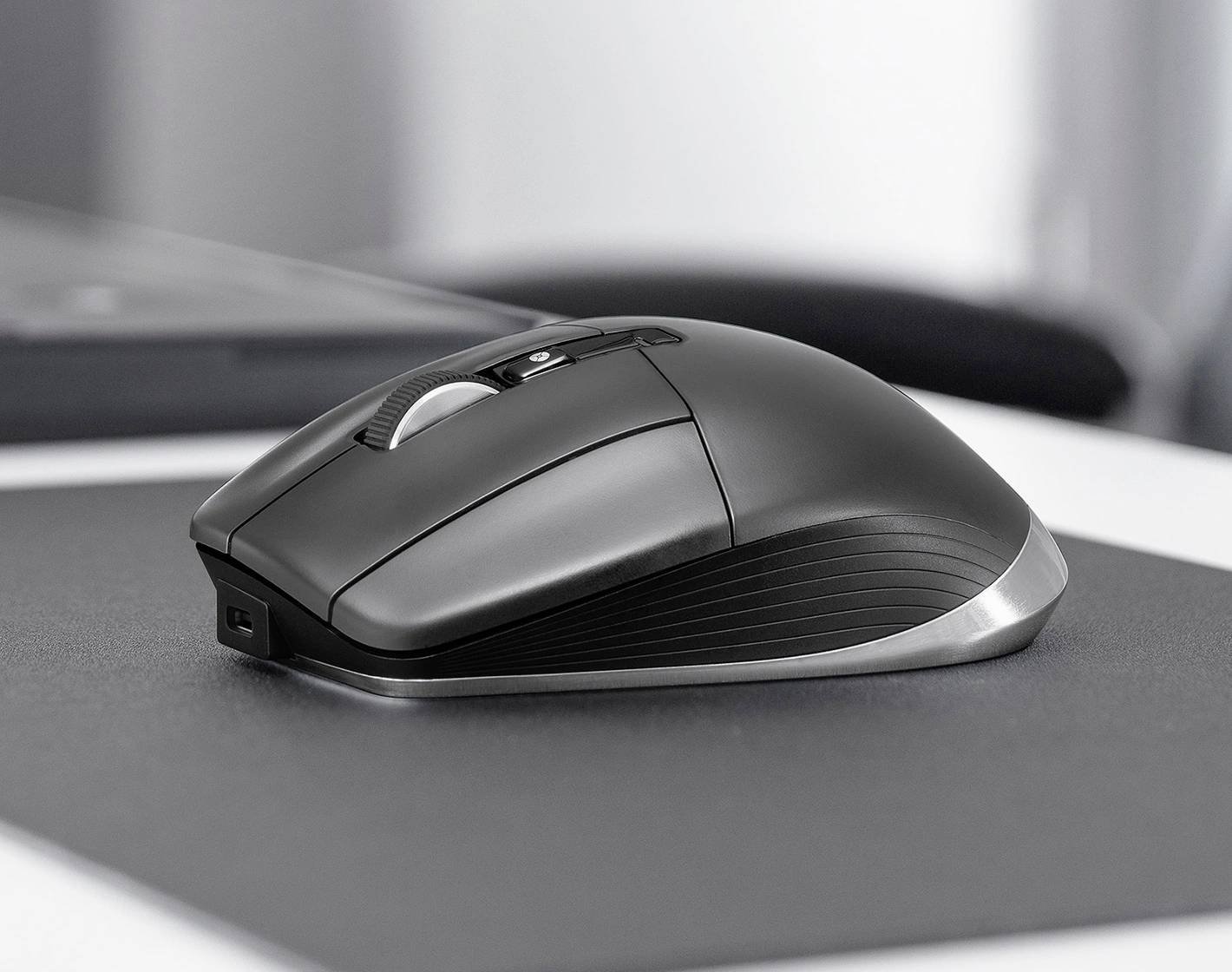 Eine schwarze kabellose Computermaus auf einer Mausunterlage, positioniert auf einem modernen Schreibtisch mit unscharfen Hintergrundelementen.