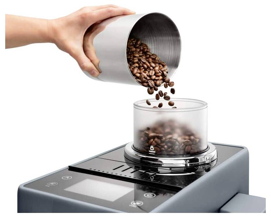 Eine Hand gießt Kaffeebohnen aus einem Metallbehälter in das transparente Fach einer Kaffeemühle auf einem eleganten, digitalen Küchentheken-Haushaltsgerät.