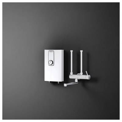Ein an der Wand montierter weißer tankloser Warmwasserbereiter mit Doppelarmatur auf dunklem Hintergrund, der sein kompaktes Design und die Rohrleitungsanlage zeigt.