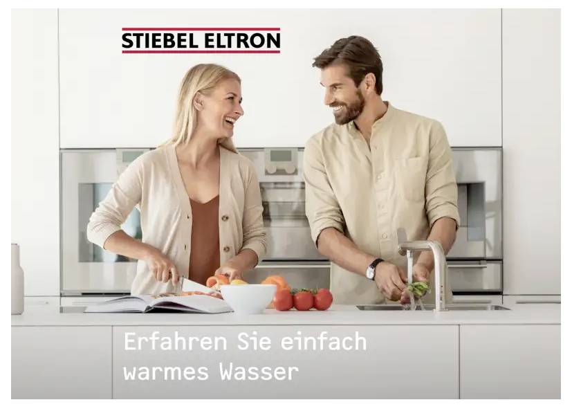 Ein Mann und eine Frau in einer modernen Küche lächeln, während sie gemeinsam Essen zubereiten. Das Bild bewirbt Stiebel Eltron, eine Marke, die mit Warmwasser verbunden ist.