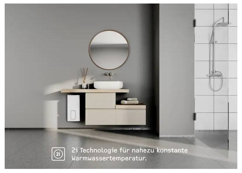 Ein modernes Badezimmer mit einem wandmontierten Waschtisch, rundem Spiegel und Duschbereich. Der Text lautet „2i Technologie für nahezu konstante Warmwassertemperatur."