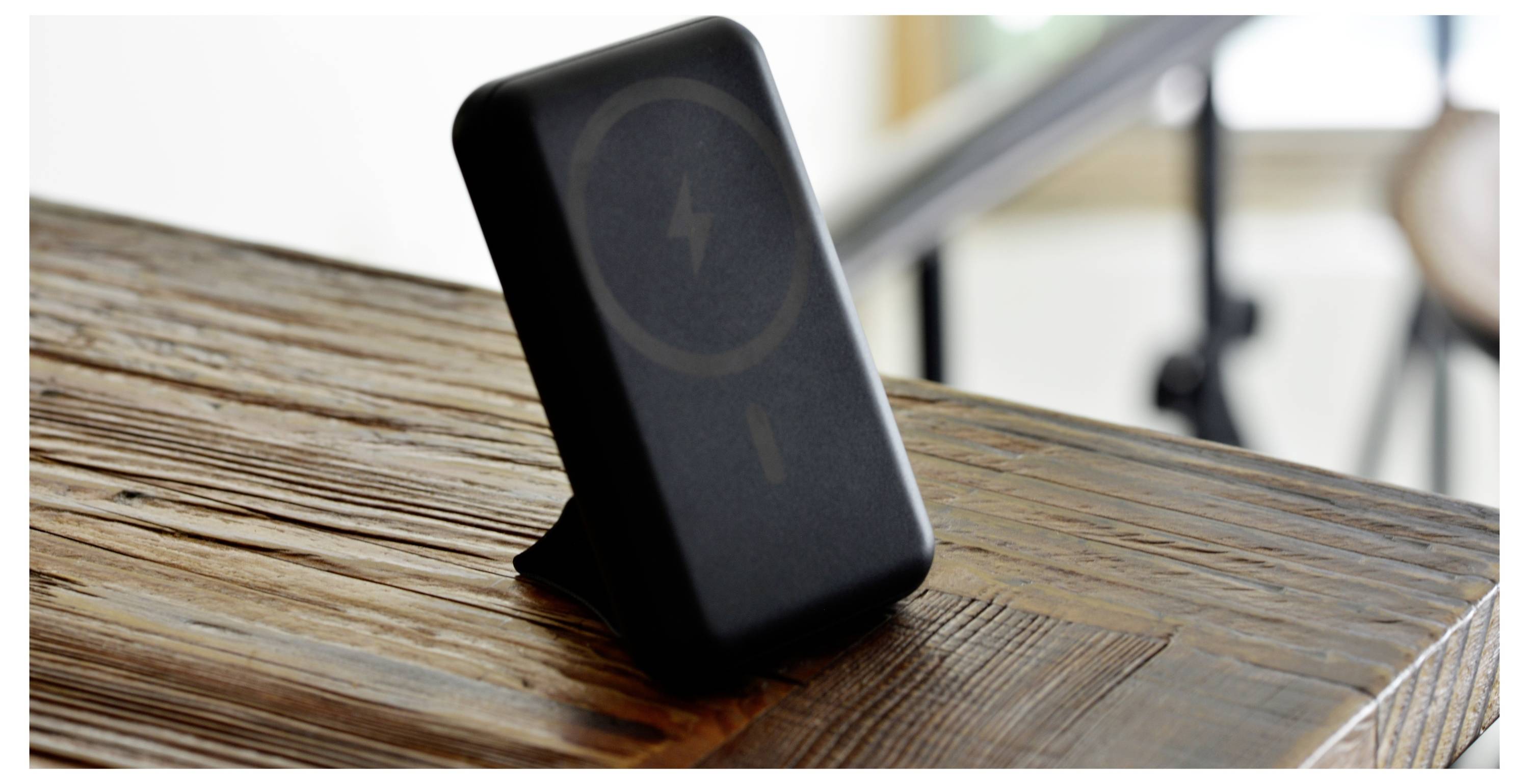 Ein schwarzes kabelloses Ladegerät mit Ständer, das ein Ladesymbol anzeigt, auf einem Holztisch platziert.