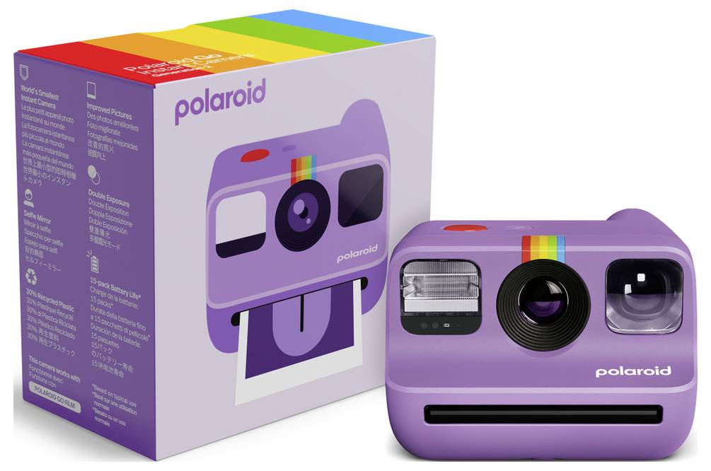 Eine lila Polaroid-Kamera mit Regenbogenstreifen ist neben ihrer passenden Schachtel positioniert. Die Verpackung zeigt Produktdetails.