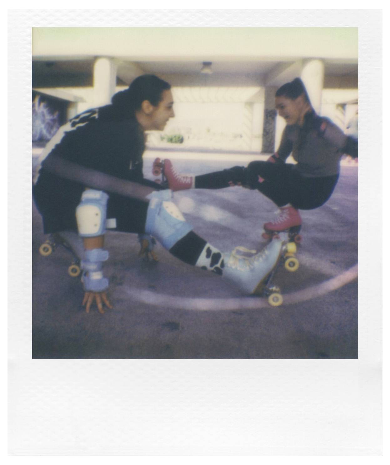 Zwei Personen fahren auf Rollschuhen in einem Unterpass und führen einen Trick auf. Eine Person hockt sich hin und hebt ein Bein an, während die andere Person auf ihr balanciert.