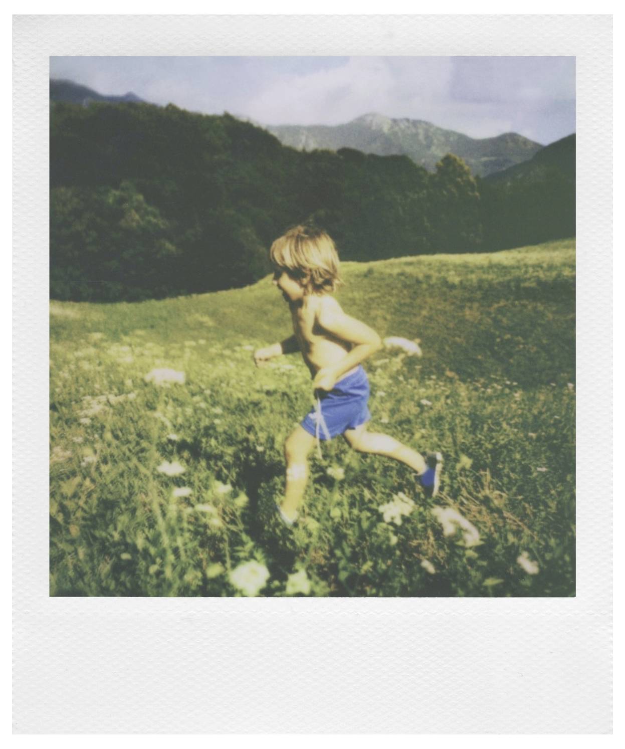 Eine weiße Sofortbildkamera mit Regenbogenfarbstreifen, Doppellinsen und einem Blitz. Das Logo „Polaroid" ist in Rot über dem Filmschlitz angebracht.