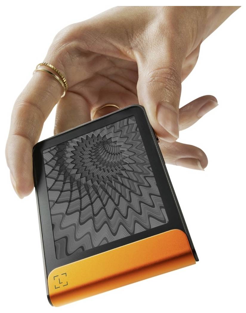 Eine Hand hält ein elektronisches Gerät mit einem Bildschirm, auf dem ein hypnotisches, spiralförmiges Schwarz-Weiß-Muster angezeigt wird. Das Gerät hat einen orangefarbenen Sockel.