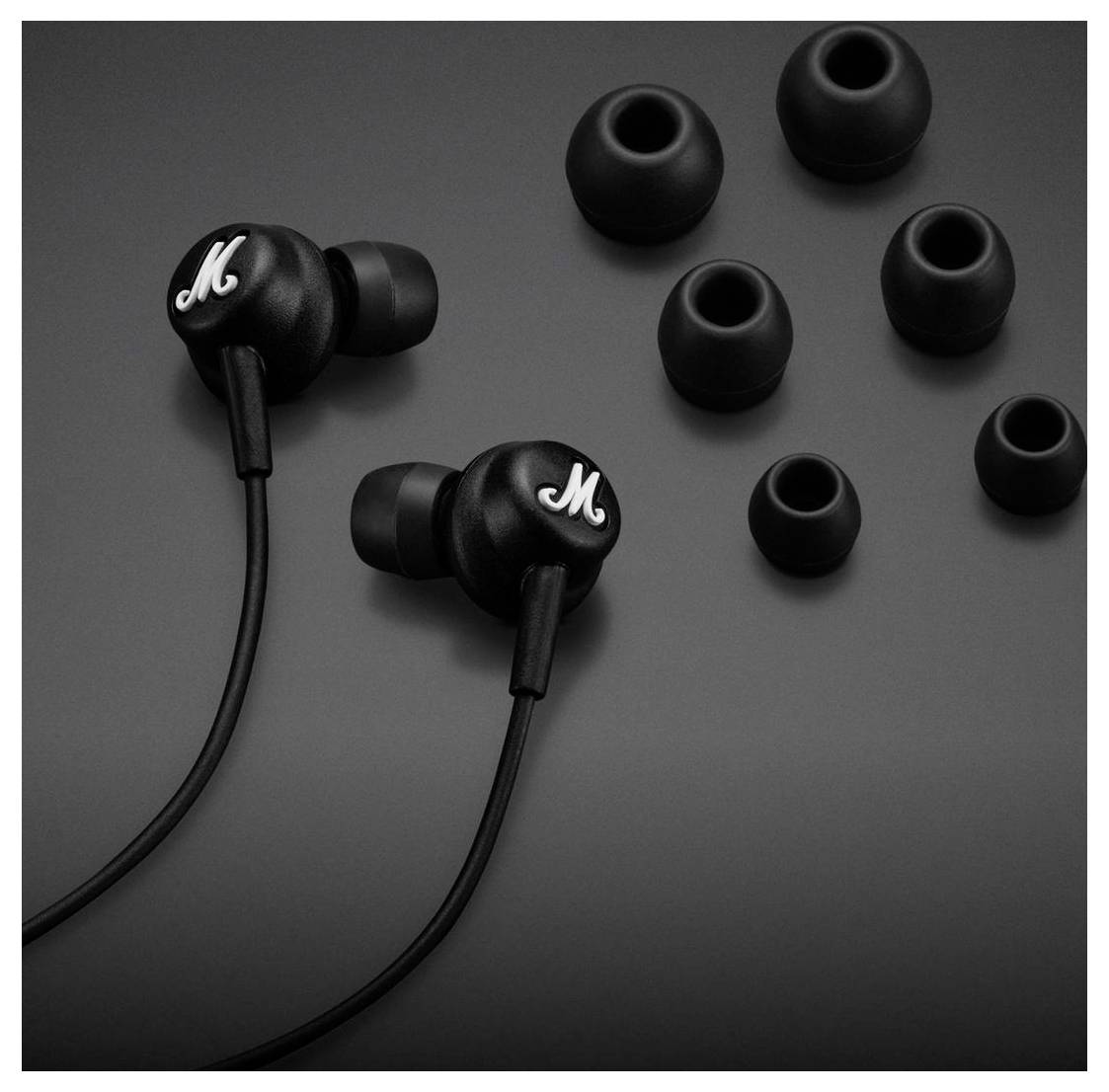 Schwarze Ohrhörer mit Logo auf matter Oberfläche, umgeben von Ohrstöpseln in verschiedenen Größen, die Anpassungsmöglichkeiten zeigen.