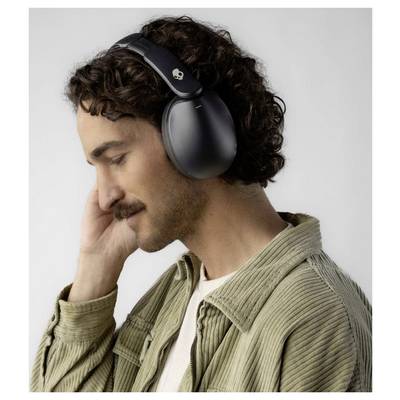Eine Person mit lockigem Haar und Schnurrbart trägt schwarze Over-Ear-Kopfhörer und hat die Augen geschlossen, was darauf hindeutet, dass sie Musik genießt.