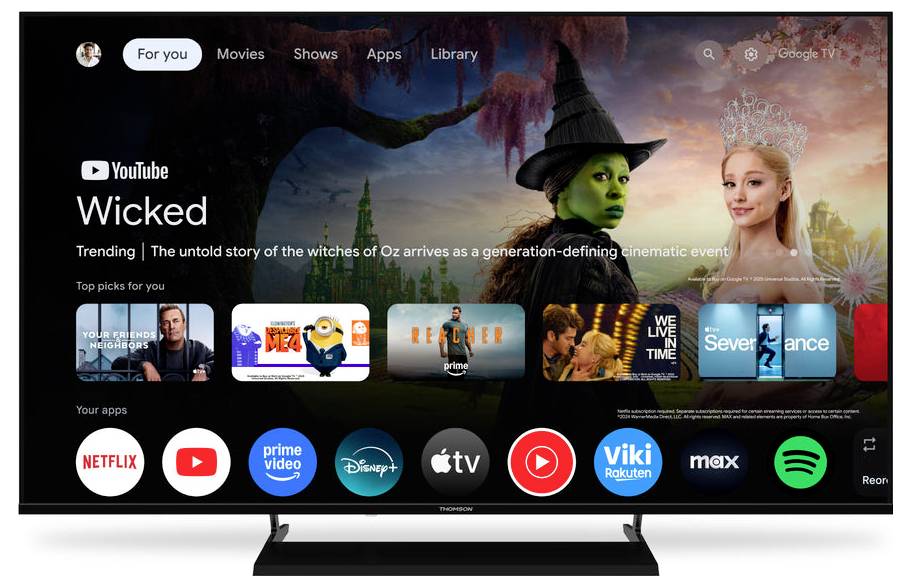 Ein Smart-TV-Interface zeigt ein Menü mit Streaming-Apps wie Netflix, Prime Video, Disney+ und YouTube an. Der hervorgehobene Bereich bewirbt „Wicked" mit Charakteren aus Oz.