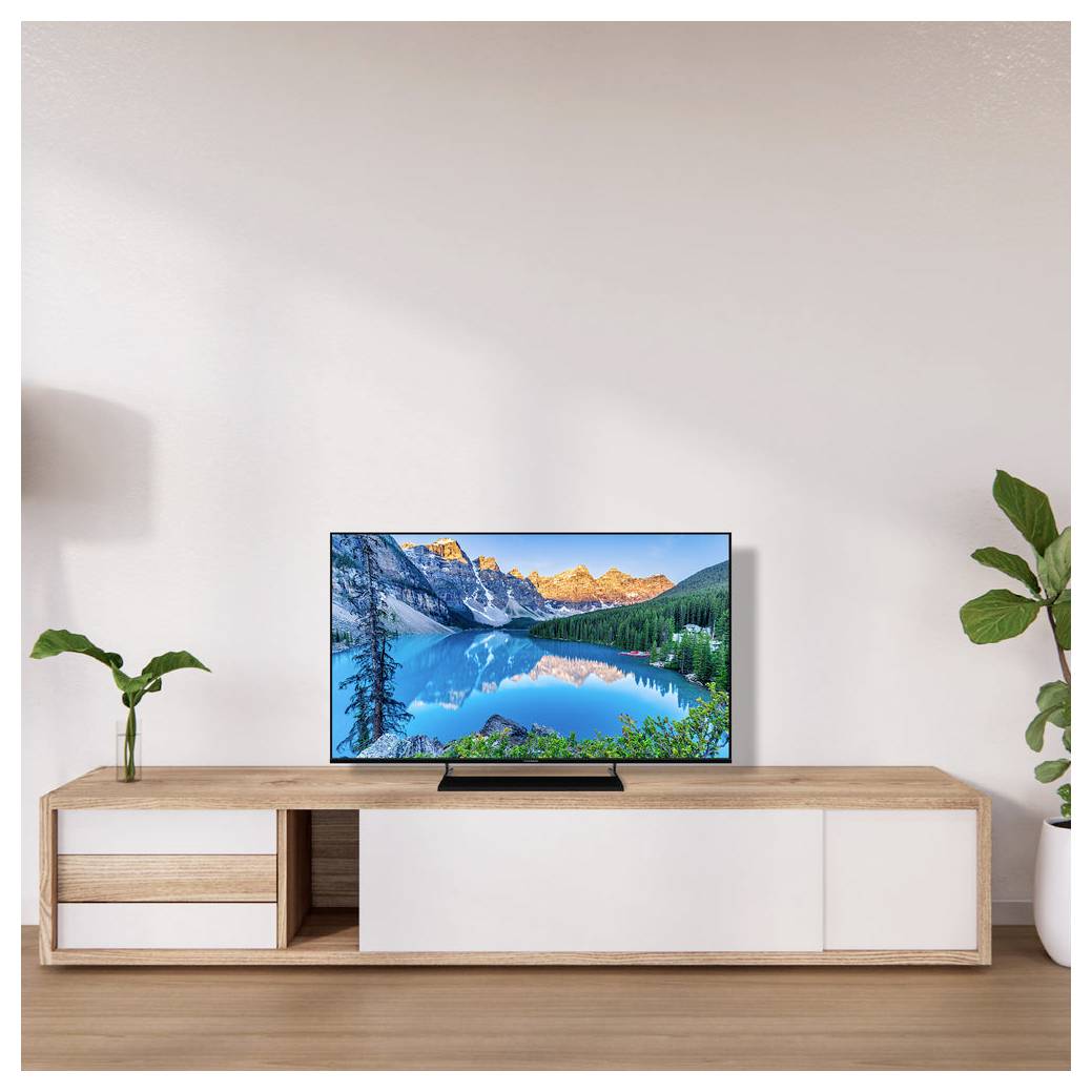 Ein modernes Wohnzimmerarrangement mit einem Flachbildfernseher auf einer Holzkonsole. Der Fernseher zeigt ein lebendiges Bild einer Bergseenlandschaft.