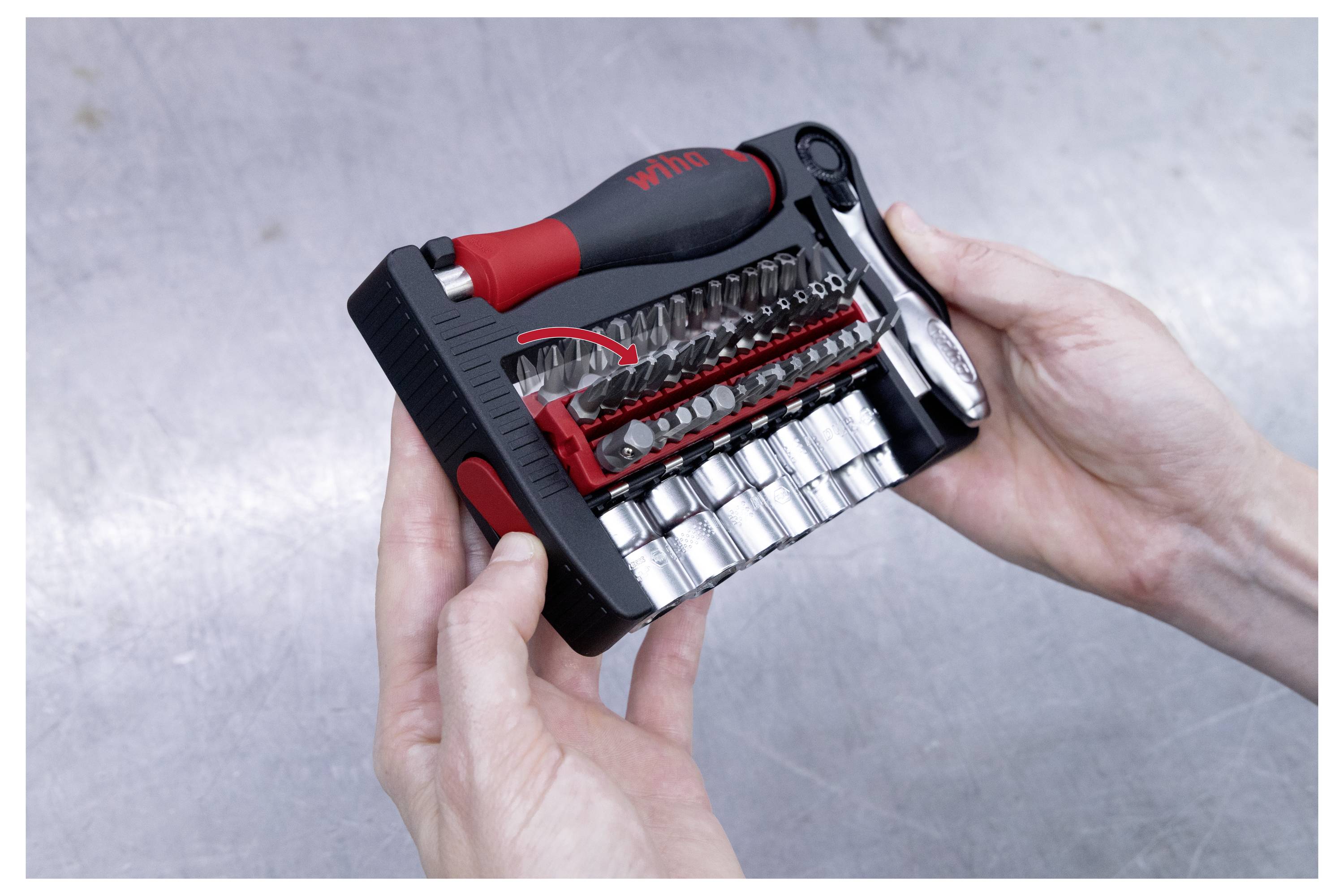 Eine Person in einer Arbeitsjacke und Hose hält einen Schraubendrehersatz in einer Tasche, steht im Freien mit unscharfem Hintergrund.